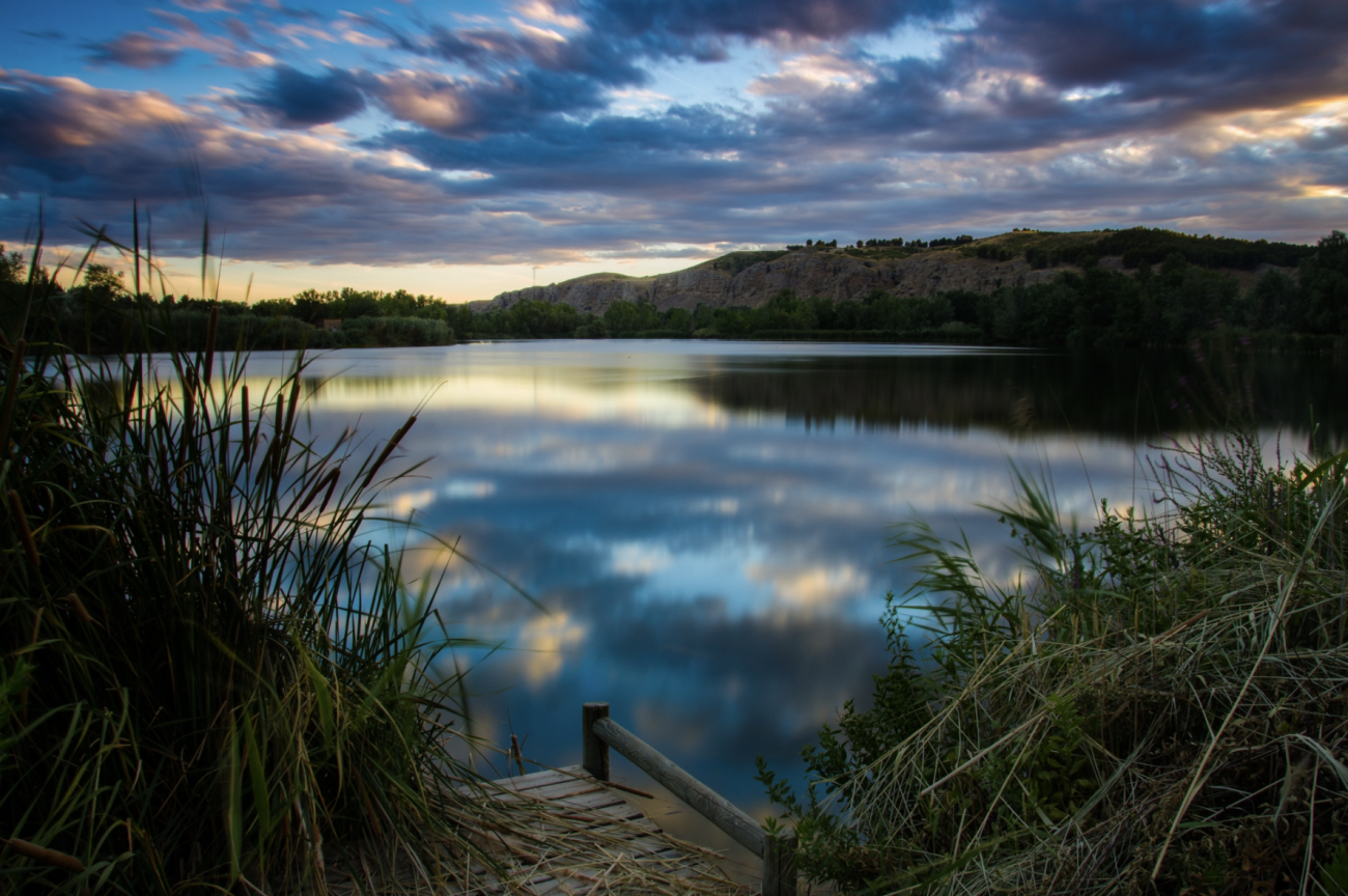 Vista de una de las lagunas del Parque Regional del Sureste, en Madrid, rodeada de vegetación y reflejos al atardecer.
