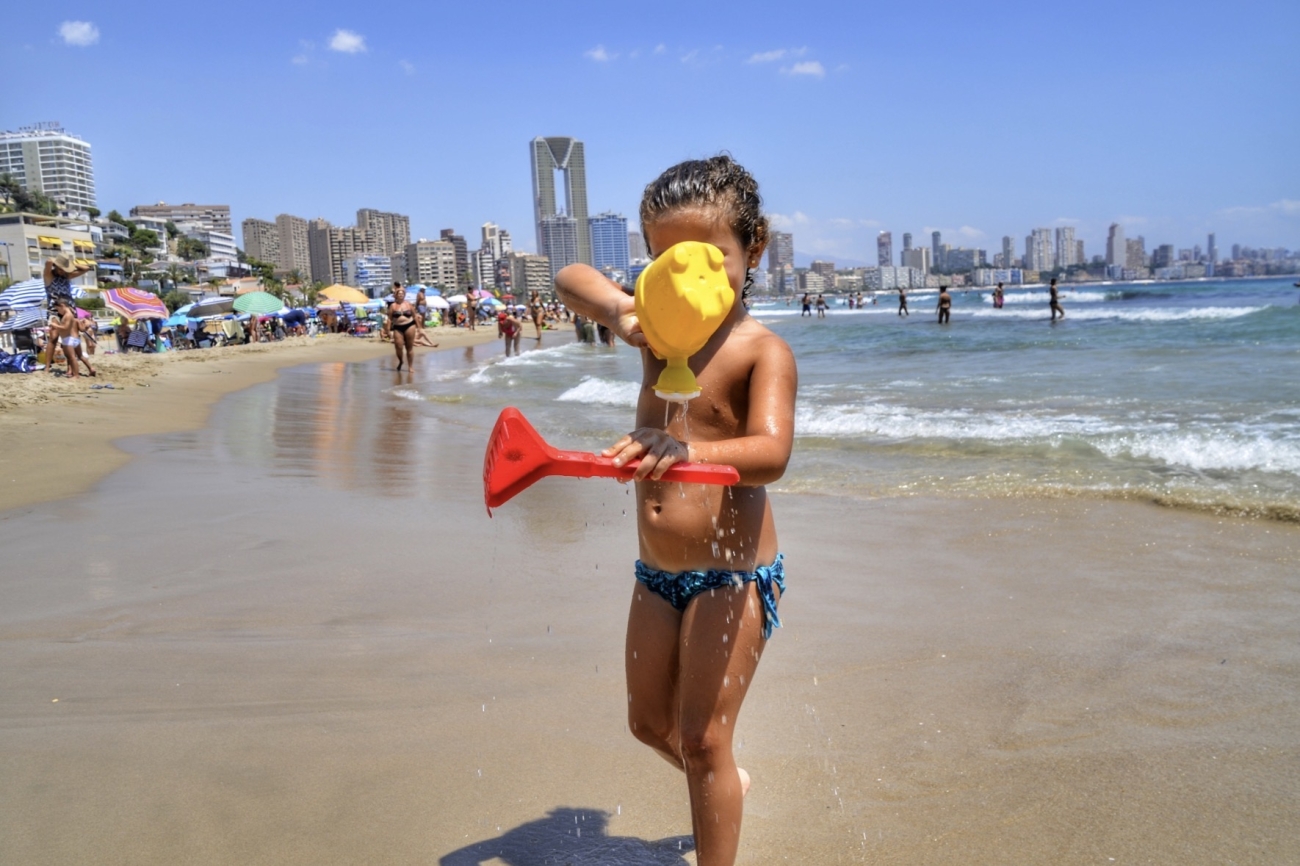 Niña jugando en una playa de Benidorm con el skyline de la ciudad al fondo, símbolo del turismo familiar y de calidad.