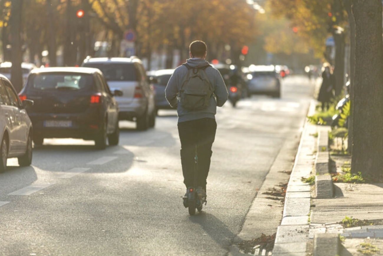 Usuario de patinete eléctrico circulando por una calle urbana junto a varios vehículos 