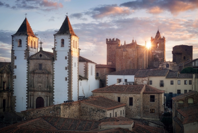 Vista panorámica del casco histórico de Cáceres al atardecer con iglesias, palacios y murallas medievales.