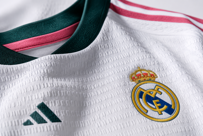 Escudo del Real Madrid sobre la nueva camiseta 2026/27 con detalles en verde y rosa y tejido blanco texturizado diseñado por Adidas. Escudo del Real Madrid sobre la nueva camiseta 2026/27 con detalles en verde y rosa y tejido blanco texturizado diseñado por Adidas.