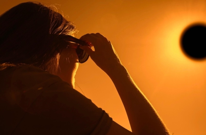 Mujer observando un eclipse solar con gafas de protección al atardecer.