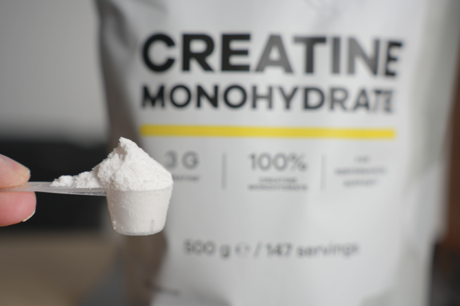 Envase de creatina monohidrato junto a una cuchara medidora con suplemento en polvo Envase de creatina monohidrato junto a una cuchara medidora con suplemento en polvo