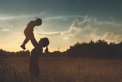 Madre alzando a su hija en brazos al atardecer en un campo, siluetas a contraluz