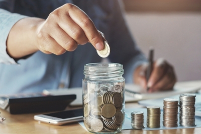 Persona introduciendo monedas en un tarro de cristal mientras los bancos vuelven a remunerar los ahorros.