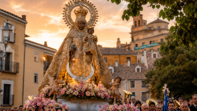 Imagen de la Virgen de la Luz en procesión por las calles de Cuenca al atardecer, rodeada de flores y fieles, con la iglesia de San Antón al fondo durante la festividad de la patrona de la ciudad.