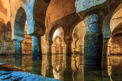 Interior del aljibe histórico de las Veletas en Cáceres con columnas y reflejos sobre el agua.