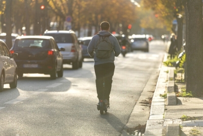 Usuario de patinete eléctrico circulando por una calle urbana junto a varios vehículos 
